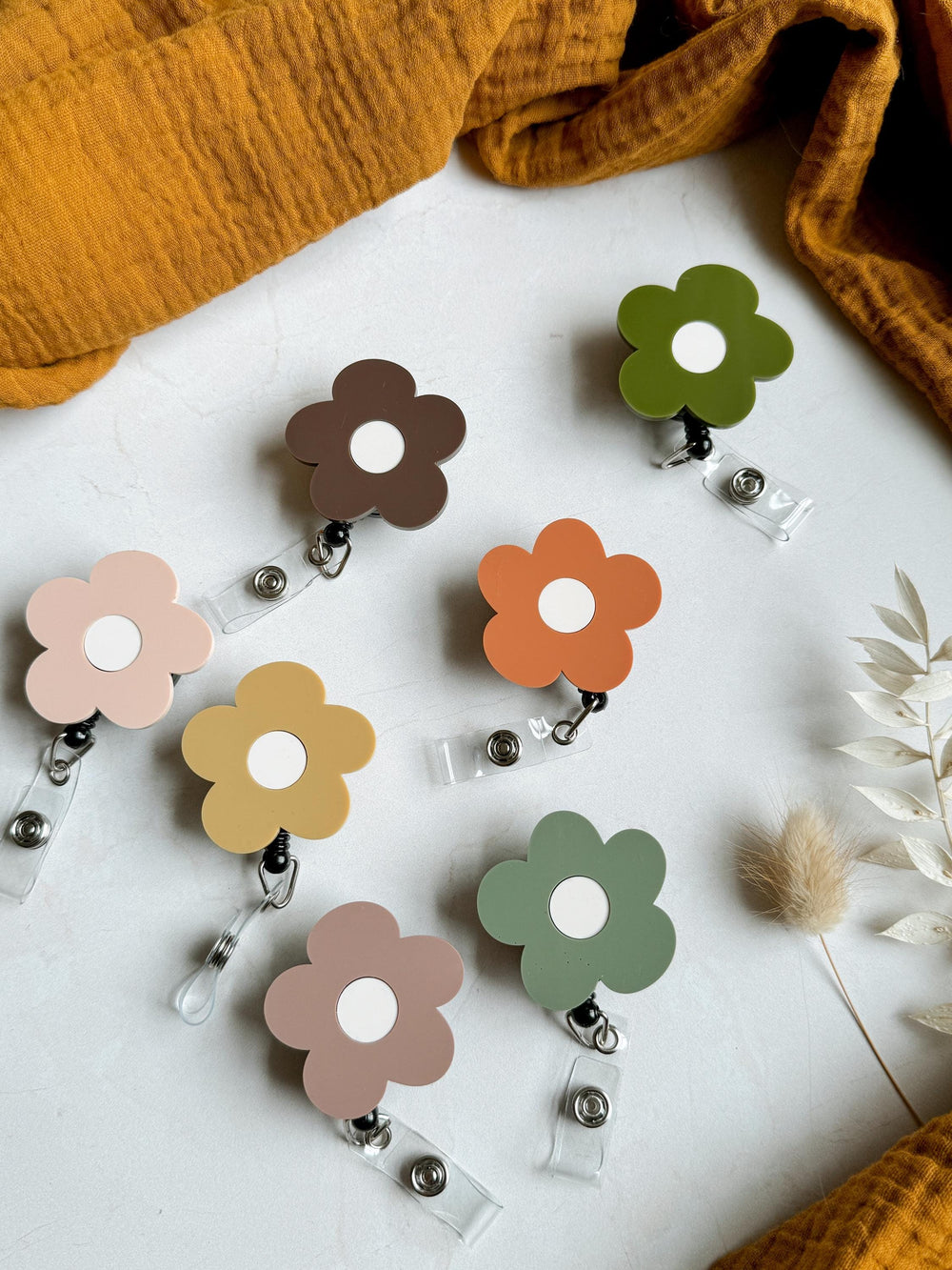 Assortment of six colorful flower-shaped retractable badge holders. Each holder features a white circle in the center and a different color: brown, orange, yellow, pink, green, and light brown.