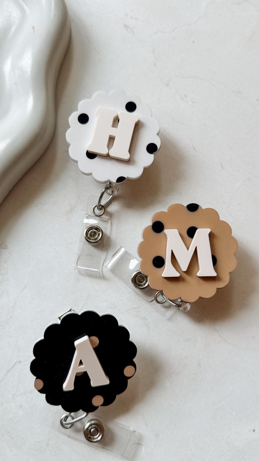 Three badge reels with different initial letters: H, M, and A. Each reel has a scalloped edge and is decorated with polka dots. The letters are in a contrasting color, and the reels have a clear plast
