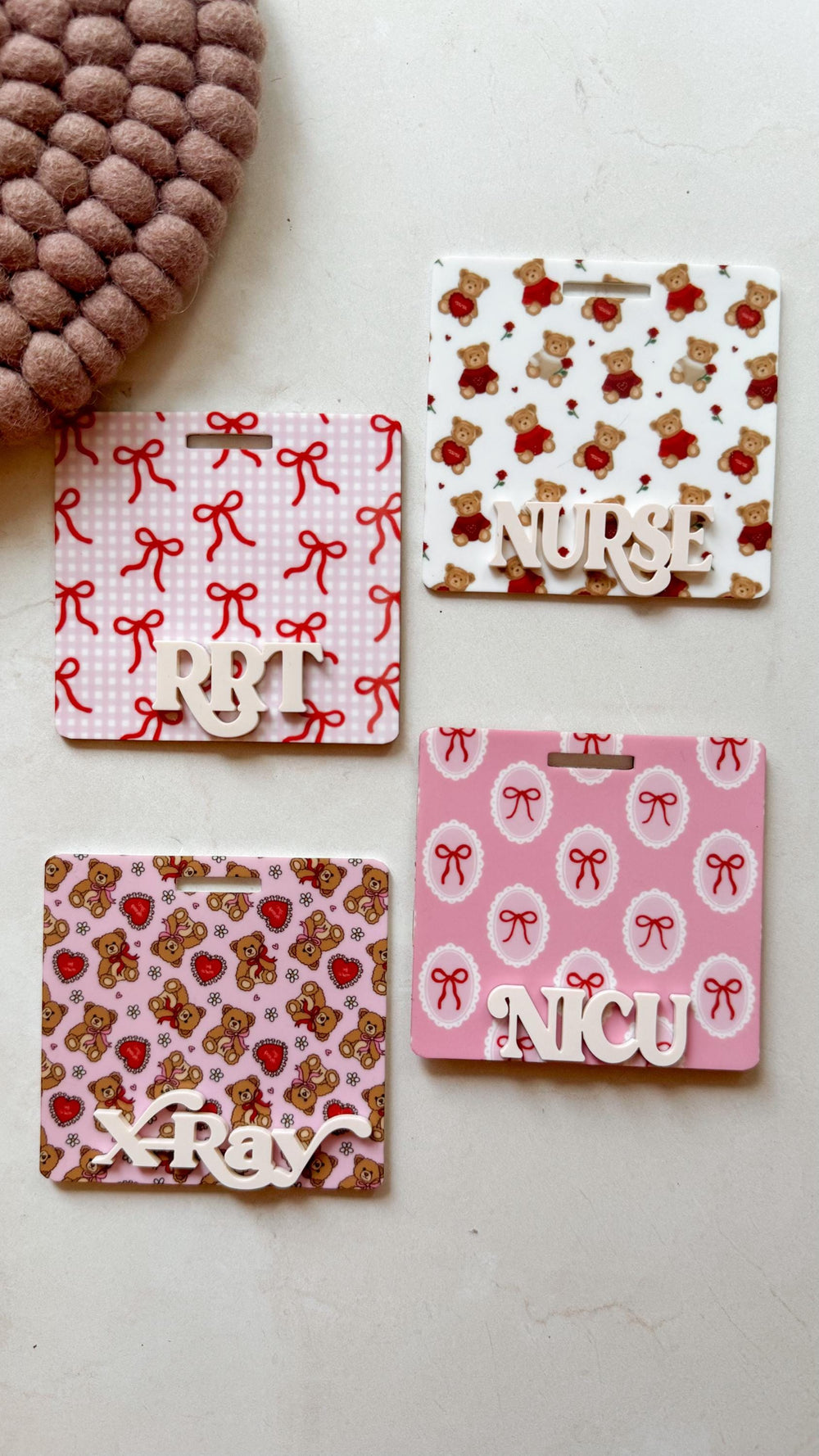 Four rectangular name badge holders with different designs. One has a pattern of red bows on a pink background with the letters "RBT". Another has teddy bears and roses with the word "". The third has