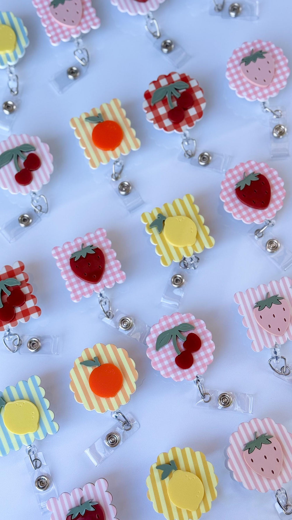 A collection of fruit-themed badge reels. The reels feature various fruit designs, including strawberries, cherries, oranges, and lemons. Each reel has a clear plastic clip and a retractable cord for 