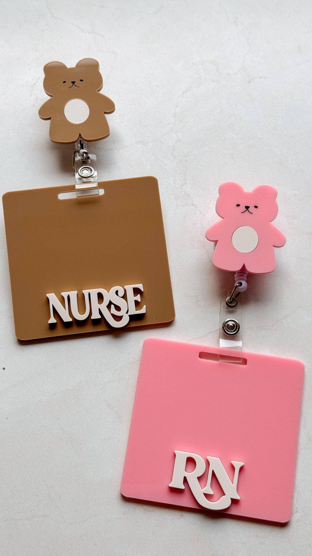 Two retractable badge holders with brown and pink bear charms. The brown badge holder has a brown background with the word "" in white letters. The pink badge holder has a pink background with the let