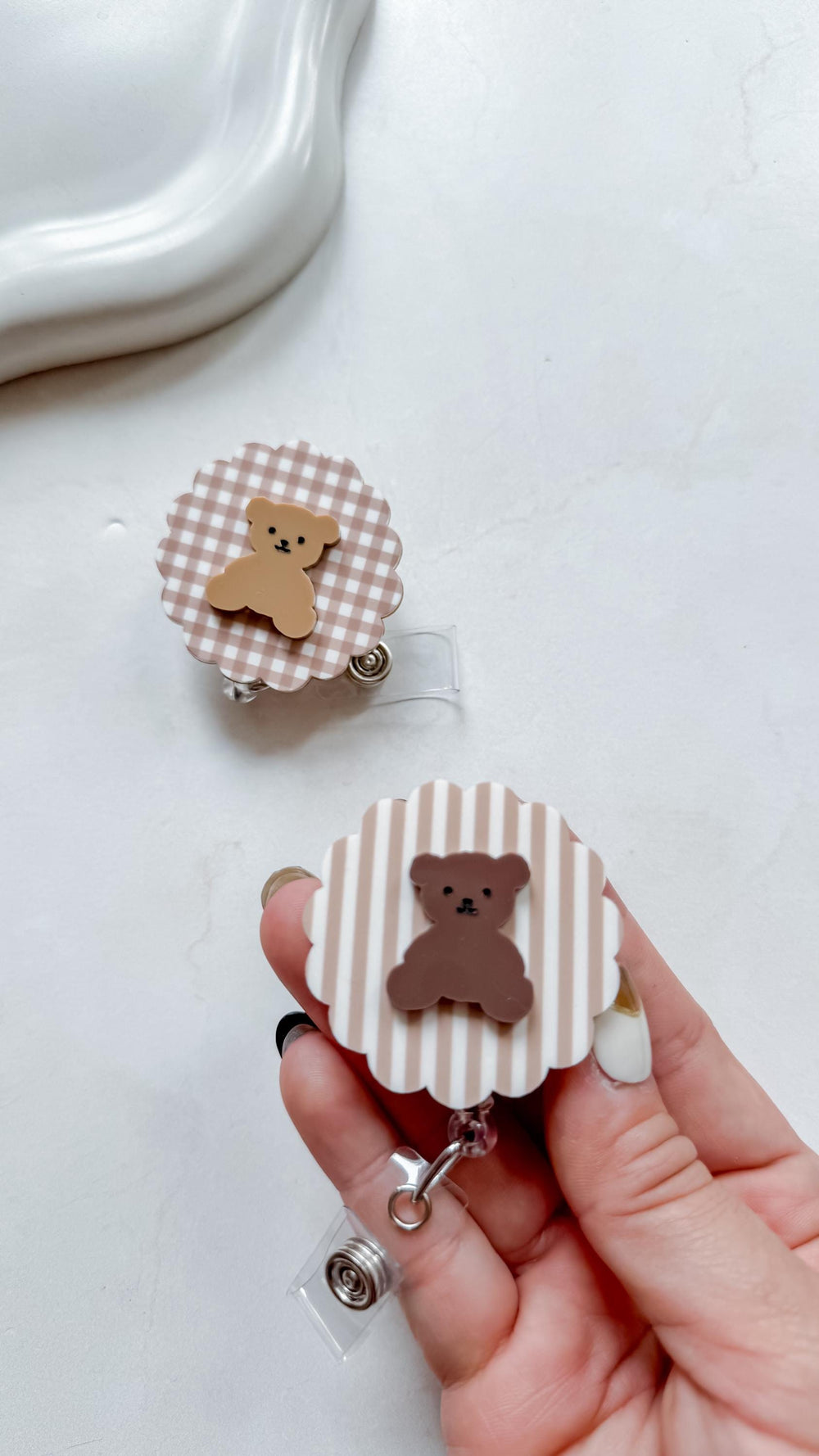 Two retractable badge holders with a teddy bear design. One has a brown and white gingham pattern, the other has brown and white stripes. Both have a brown teddy bear in the center.