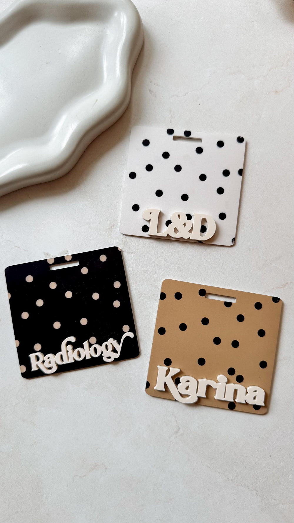 Three name tags with a polka dot pattern. One is black with white dots and the word "". Another is white with black dots and the letters "". The third is tan with black dots and the name "Karina".