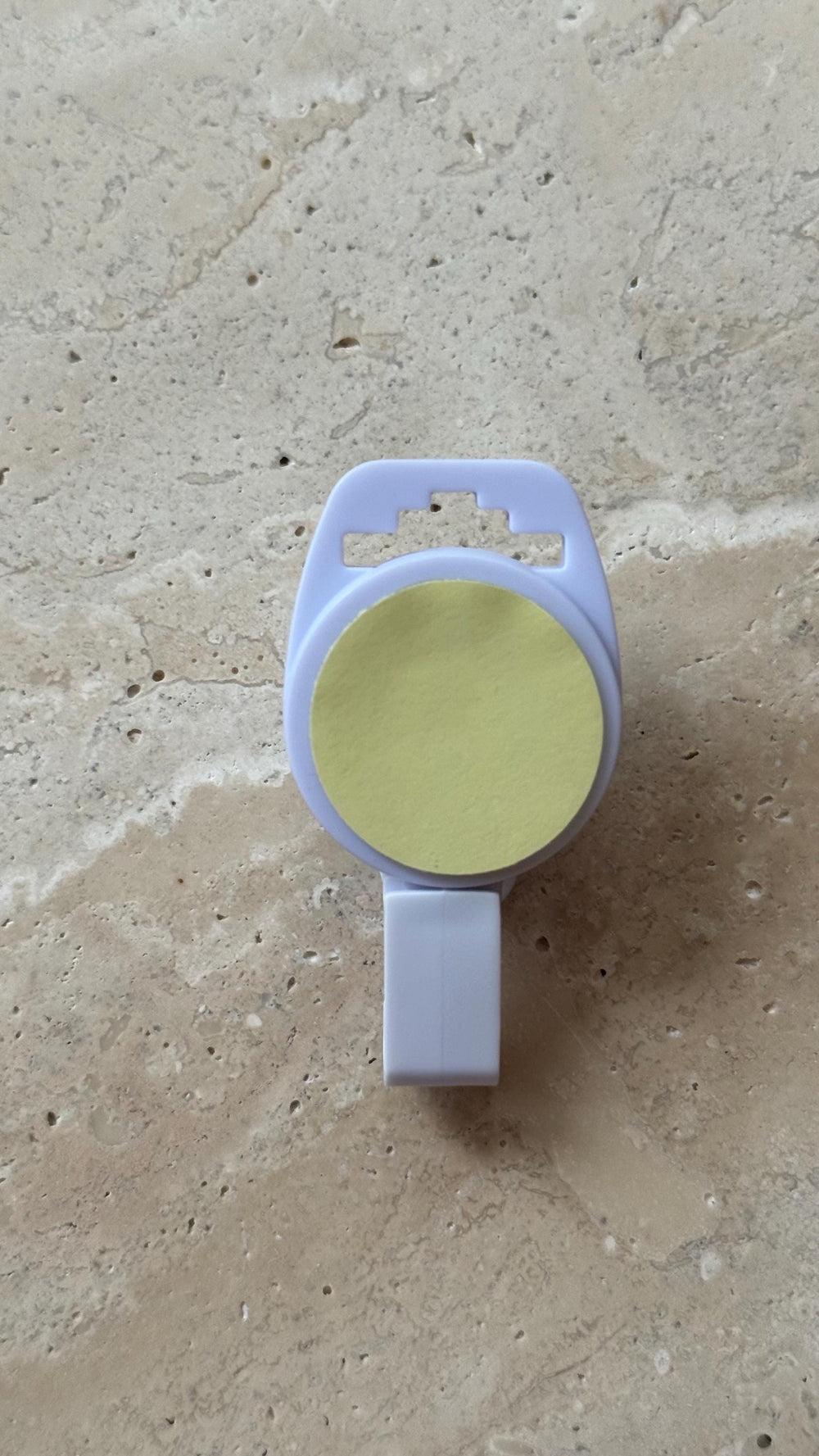 A light purple, plastic tag holder with a yellow circular sticker. The holder has a rectangular base and a top section with a hole for hanging. The sticker is centered on the holder.