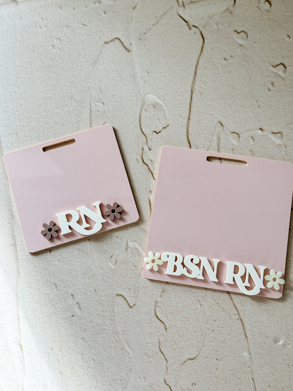 Two pink plastic name tags with white letters and flowers. The top tag says "" and the bottom tag says "BSN ".