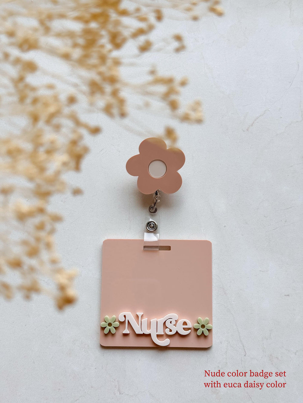A pink badge holder with the word "" in white letters and two green flowers on either side. The badge holder is attached to a retractable badge reel with a pink flower charm.