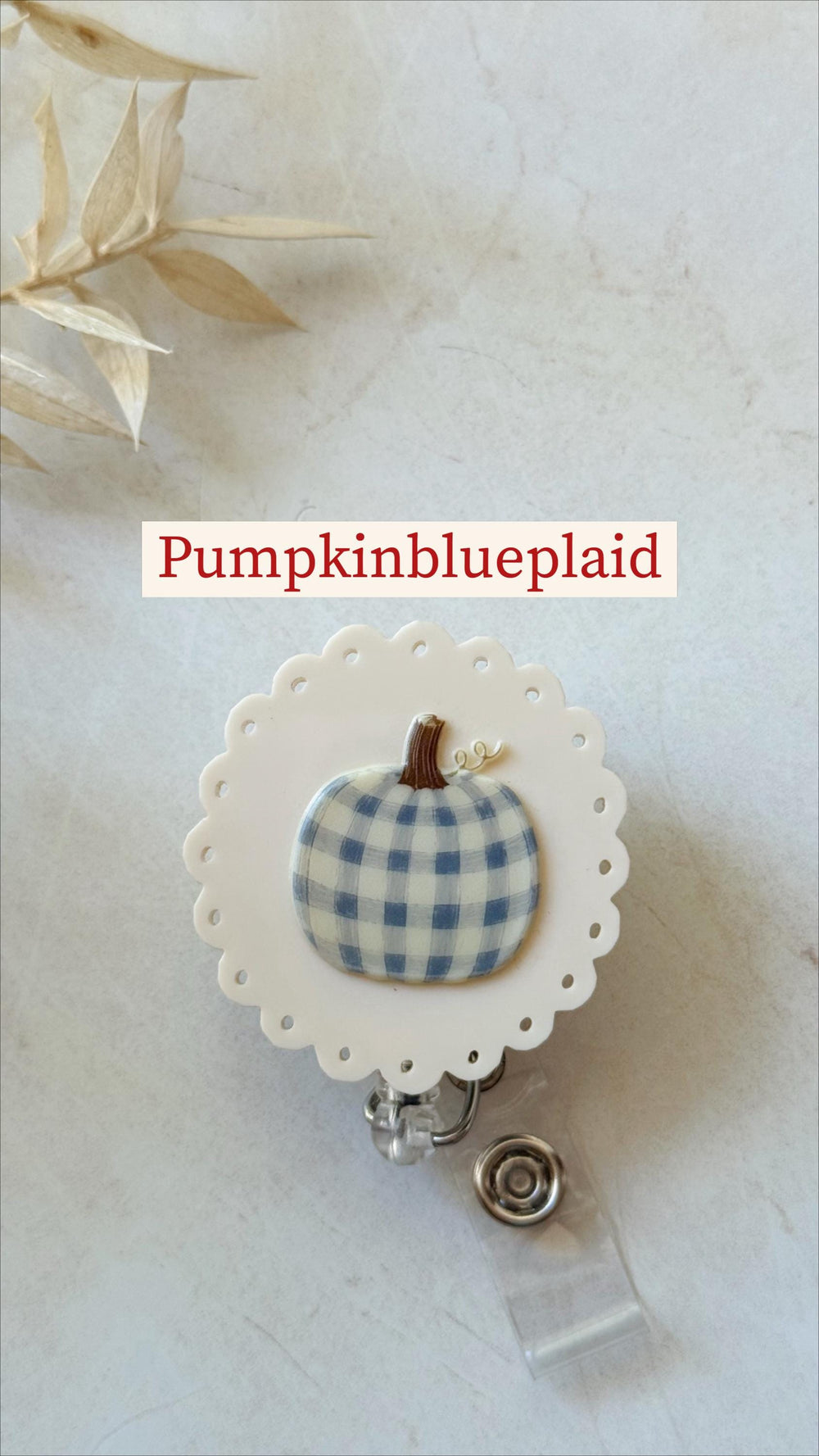 A round badge reel featuring a white scalloped edge and a central graphic of a blue and white plaid pumpkin with a brown stem. The text Pumpkinblueplaid is displayed above the badge reel, which includ