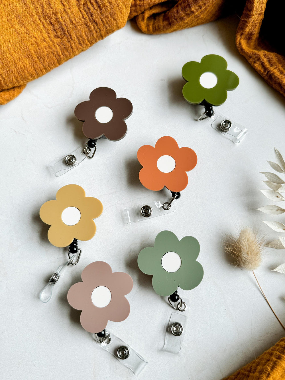 Five colorful flower-shaped retractable badge holders with white centers. The colors are brown, orange, yellow, green, and pink.