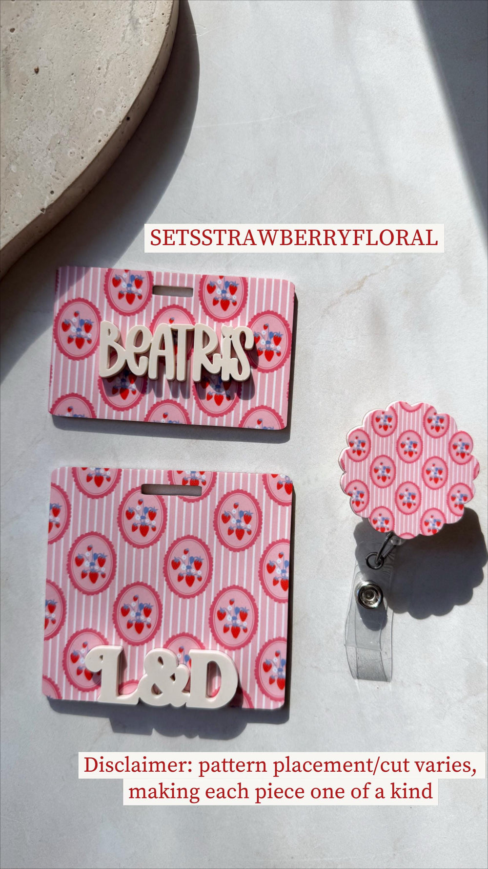 Pink and white badge holders with a strawberry and floral pattern. One badge holder has the name "BEATRIS" in white letters, and another has the letters "". A matching retractable badge reel is also s