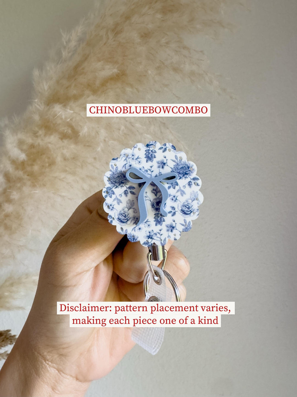 A round badge reel with a blue floral pattern and a light blue bow. The badge reel has a scalloped edge and a silver clip. The text "CHINOBLUEBOWCOMBO" is at the top. The text "Disclaimer: pattern pla