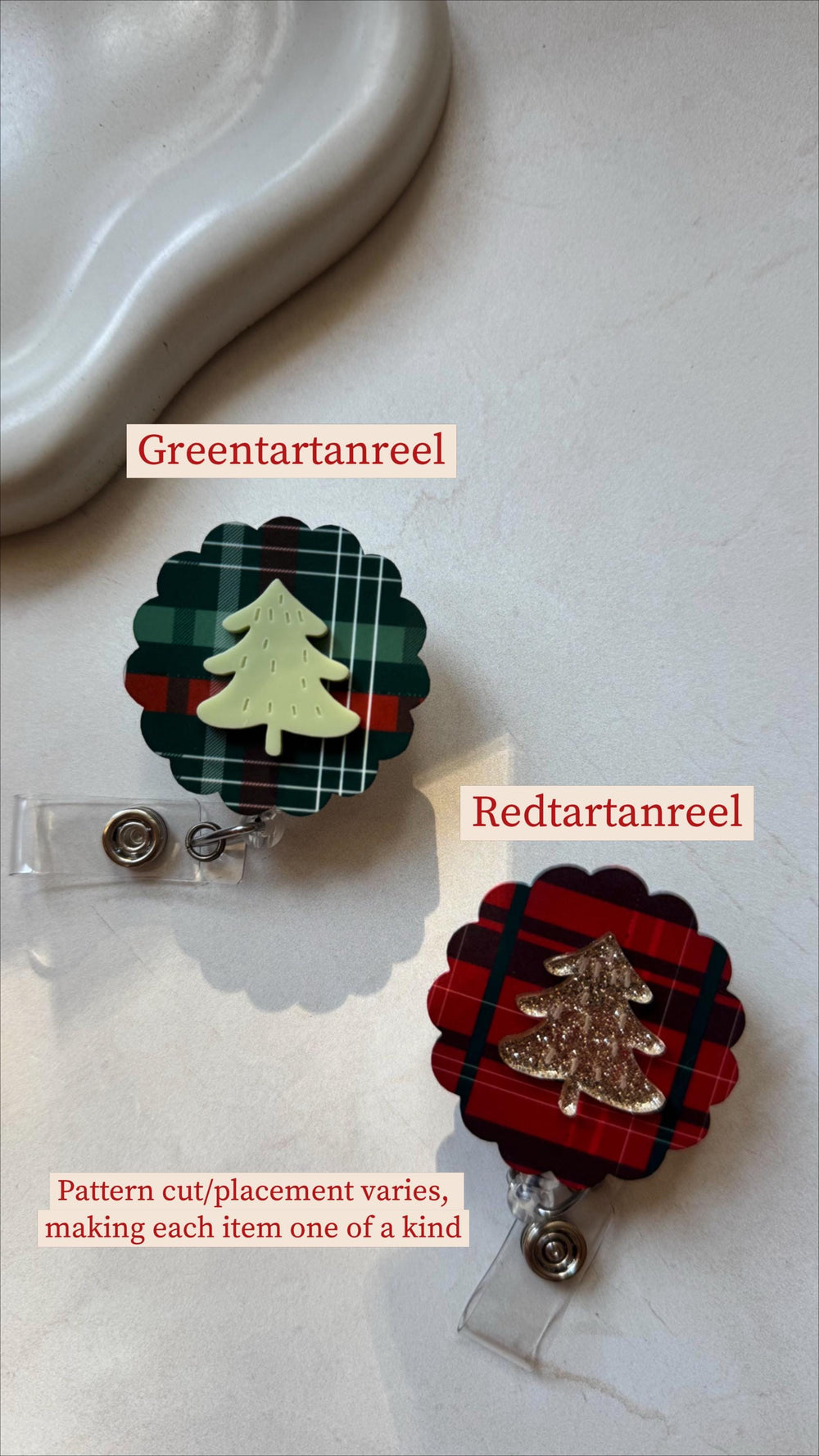 Two Christmas-themed badge reels. One features a green and red plaid pattern with a light green tree, the other has a red and black plaid pattern with a gold glitter tree. Each reel has a clear plasti