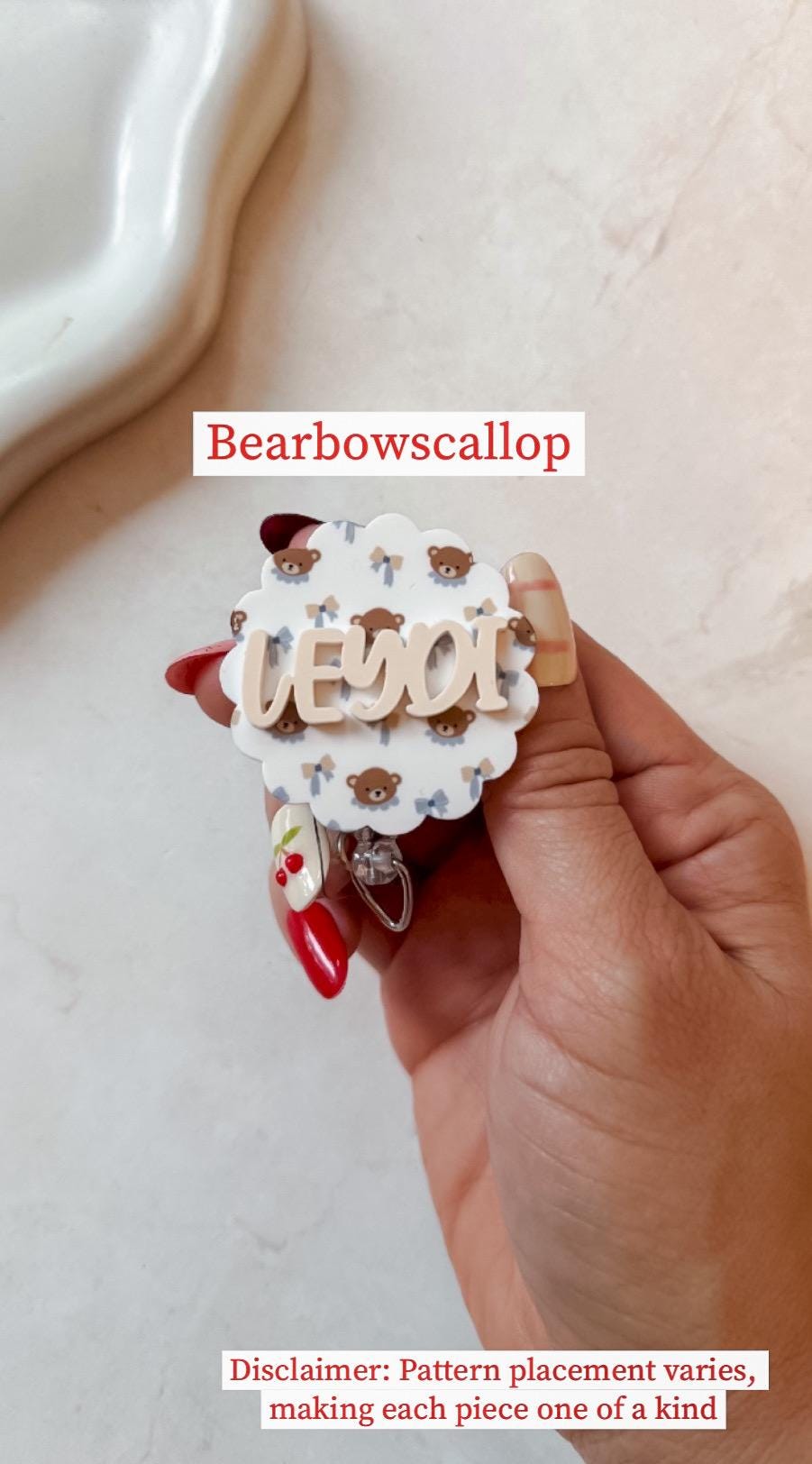 A white and light blue badge reel with a cloud shape and a teddy bear pattern. The name "LEYDI" is in a light brown color. The text "Bearbowscallop" is at the top.