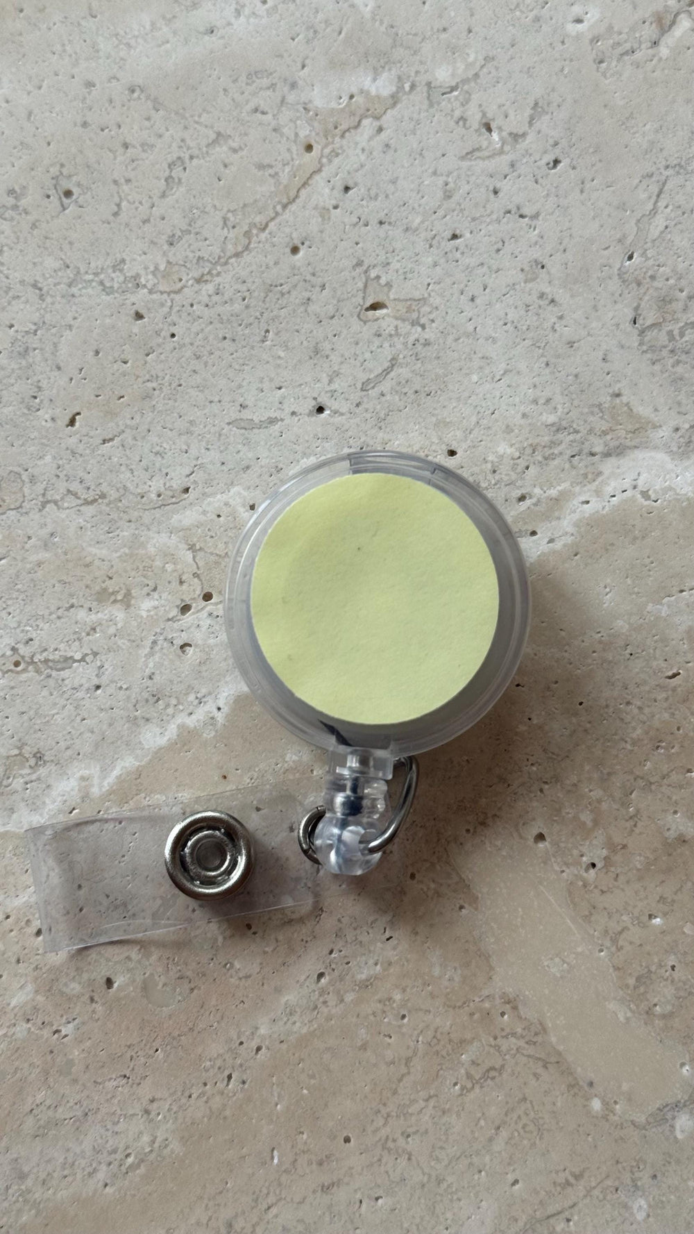 A clear plastic retractable badge reel with a yellow circular insert. The reel has a clear plastic strap with a metal snap closure. The reel is designed to hold an  or similar item.