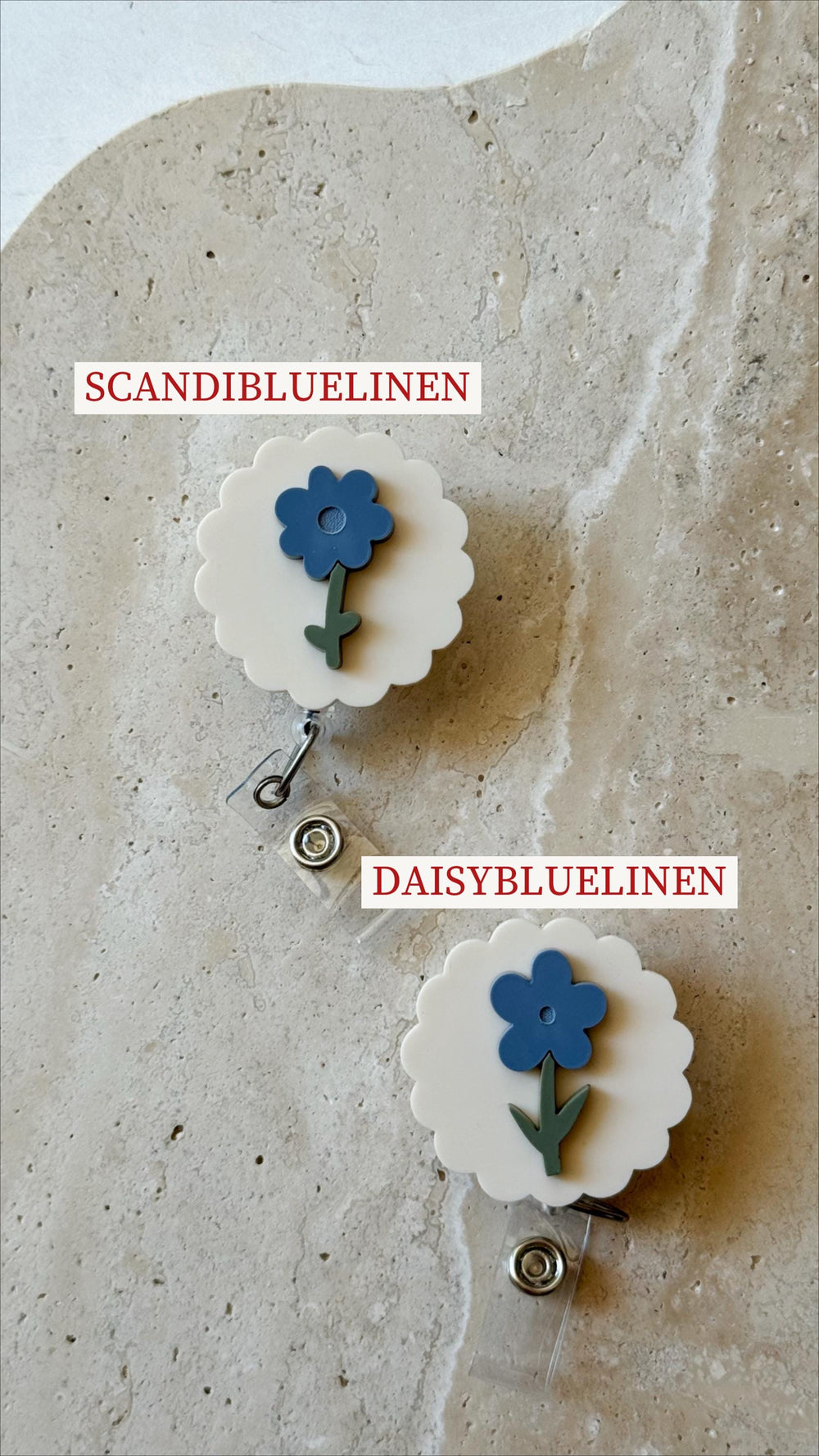 Two white badge reels with a scalloped edge, each featuring a blue flower design with a green stem. The text "SCANDIBLUELINEN" and "DAISYBLUELINEN" are printed on the image. These are likely for holdi