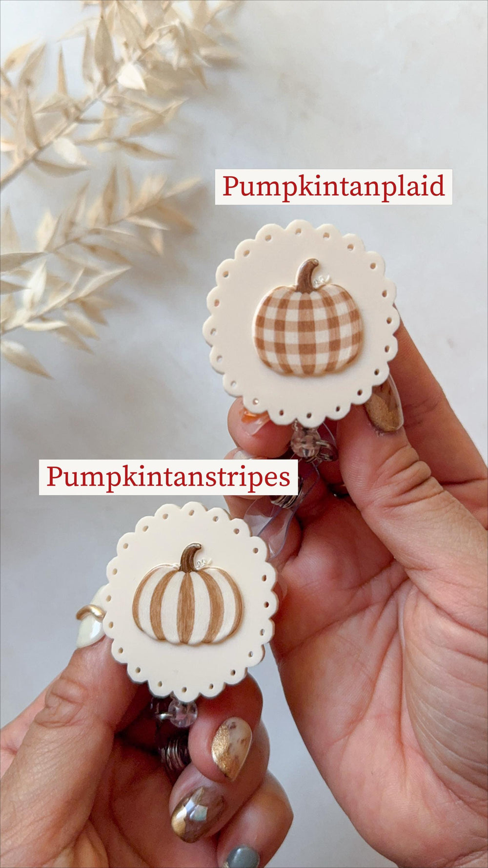 Two round badge reels with scalloped edges and cream-colored bases. One features a brown and white plaid pumpkin with the text Pumpkintanplaid, and the other features a brown and white striped pumpkin