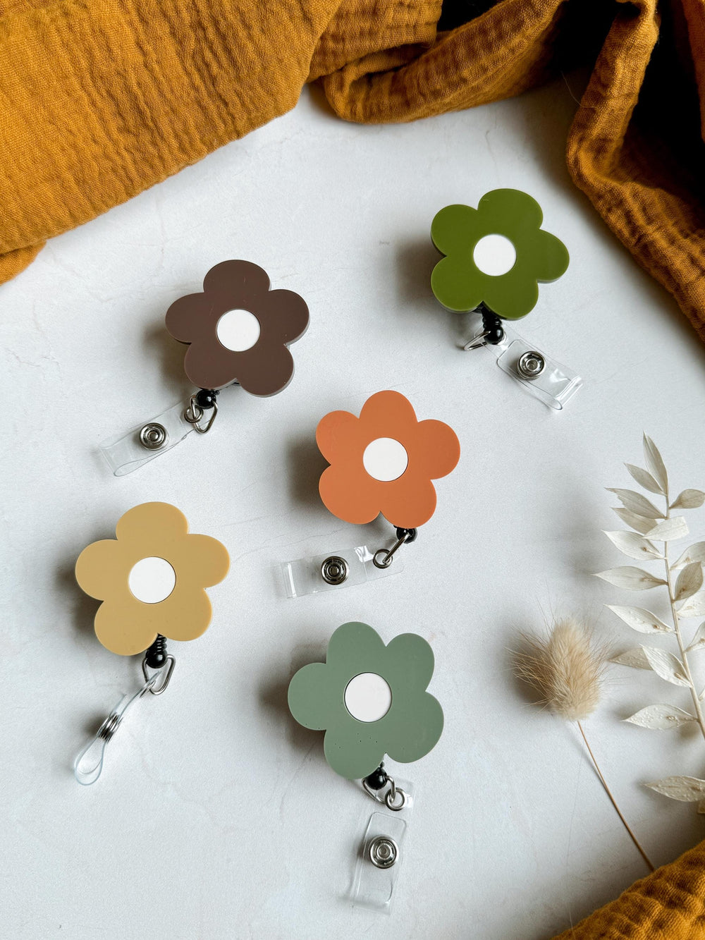 Five colorful flower-shaped retractable badge holders with white centers. The holders are in shades of brown, orange, green, and yellow.