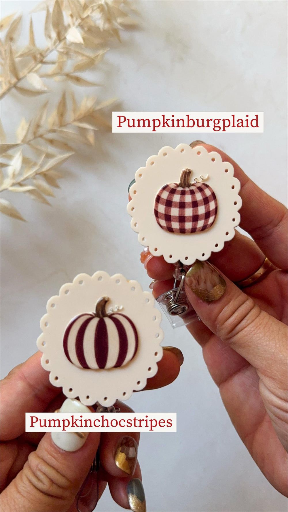 Two round badge reels with scalloped edges and cream-colored backgrounds. One features a brown and white plaid pumpkin labeled Pumpkinburgplaid, and the other displays a dark brown striped pumpkin lab