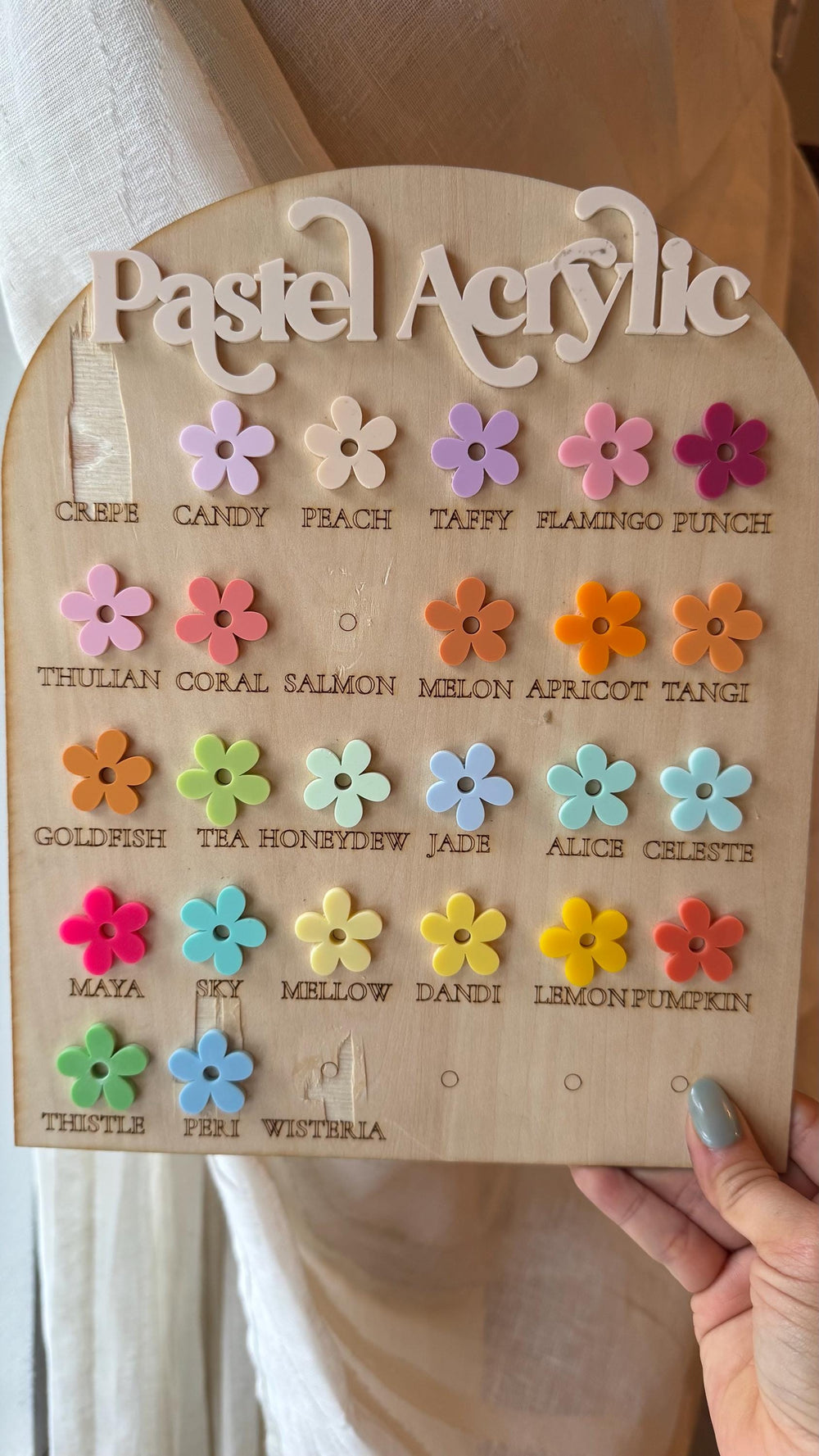A wooden display board with the words "Pastel Acrylic" and a series of colorful acrylic flower samples. The flowers are in various pastel shades, with names like "Crepe," "Candy," and "Peach" below ea