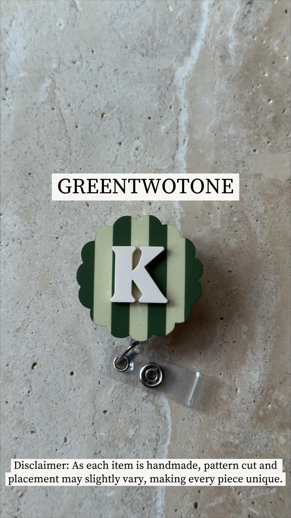 A badge reel with a green and white striped design, featuring a white letter "K". The badge reel has a scalloped edge and a clear plastic strap with a metal clip. The text "GREENTWOTONE" is at the top