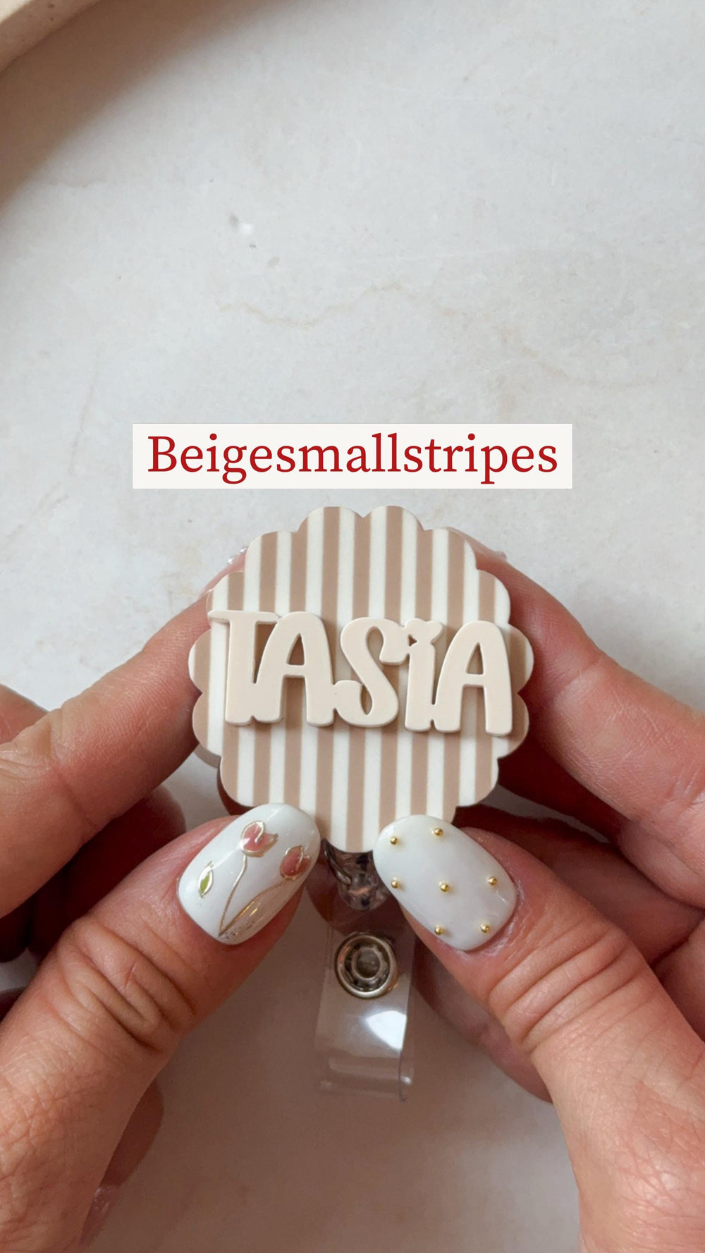 A beige and white badge reel with the name "TASIA" in a beige font. The badge reel has a striped background and a scalloped edge. The text "Beigesmallstripes" is above the badge reel.
