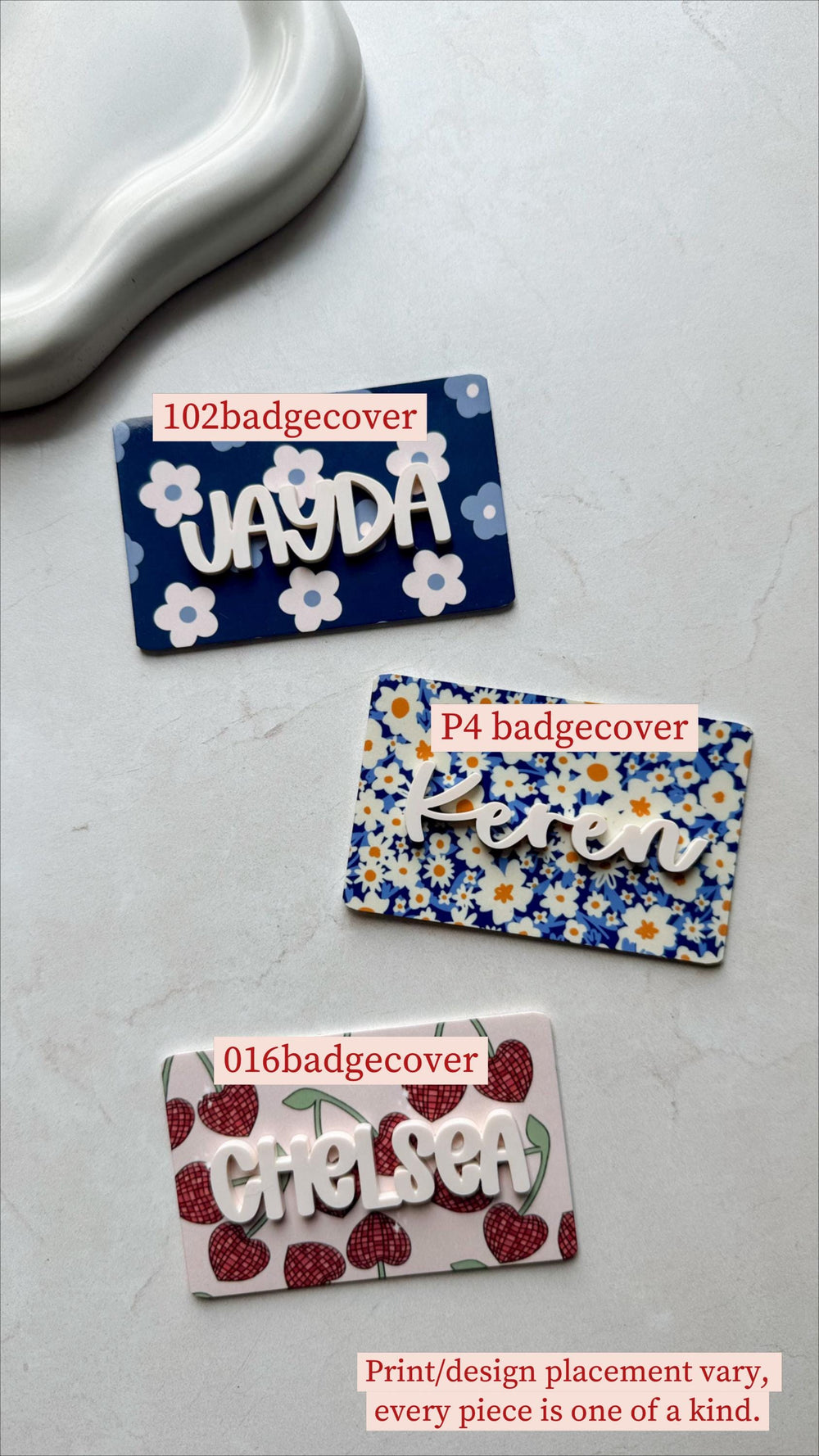 Three name badge covers with white lettering. One is navy blue with white flowers and the name "Jayda". Another is floral with the name "Keren". The last is pink with cherries and the name "Chelsea".