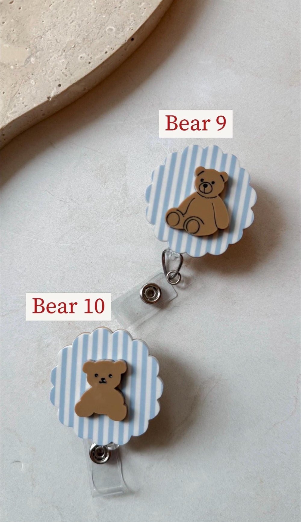 Two badge reels with a light blue and white striped background and a brown teddy bear design. The text "Bear 9" and "Bear 10" are printed on the image. Each reel has a clear plastic strap and a metal 
