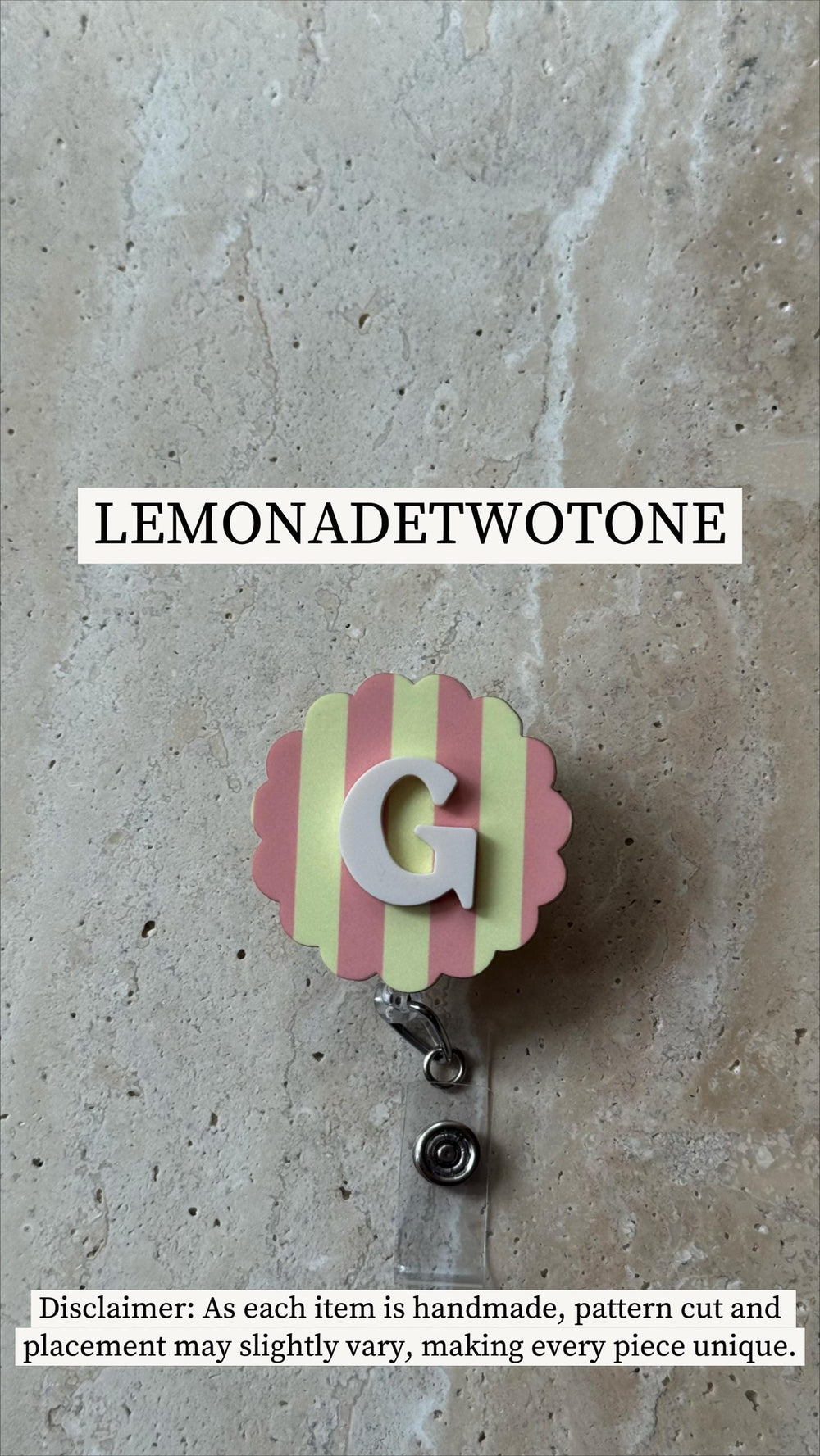 A badge reel with a pink and yellow striped scalloped edge, featuring a white letter "G". The text "LEMONADETWOTONE" is above the badge. The reel has a clear plastic strap and a metal clip.