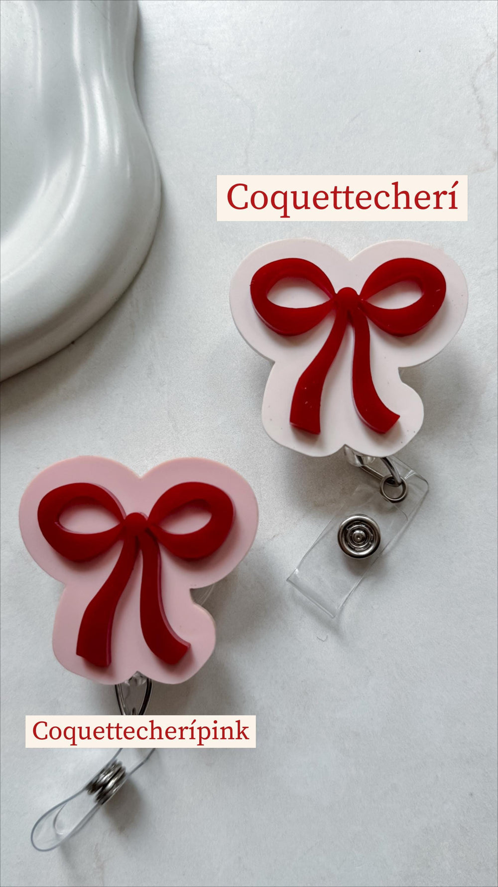 Two badge reels with red bow accents. One is pink and the other is white. The text "Coquettecherí" and "Coquettecherípink" are printed on the image. Each reel has a clear plastic strap and a metal cli